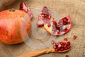 Ripe juicy pomegranate, pieces of pomegranate, pomegranate seeds on a wooden spoon on a background of rough homespun fabric. Close