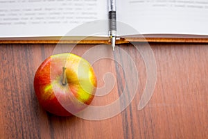 Ripe juicy red apple near the book and pen. Useful food during a