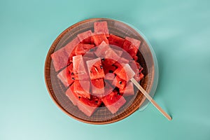 Ripe juicy red watermelon cubes in a brown clay plate on blue background. Watermelon cubes ready for eat