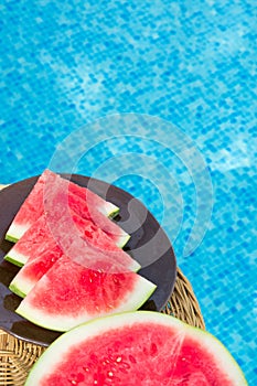 Ripe Juicy Seedless Watermelon Cut in Slices Wedges on Plate on Rattan Table by Swimming Pool. Sunlight. Vacation