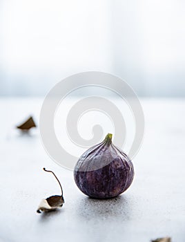 Ripe juicy single fig on a white table near the window. Morning light