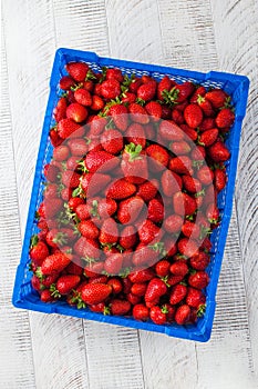 Ripe juicy strawberries in a plastic box on a wooden table. Berries, harvesting.