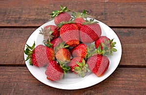 Ripe juicy strawberries on a white plate - a delicious dessert. A wooden background.