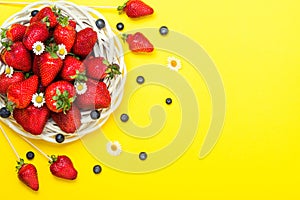 Ripe juicy strawberries in a wicker white basket and blueberries on a colored background.