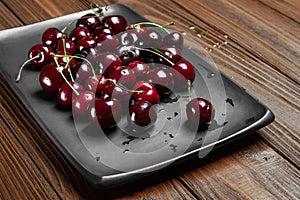 Ripe juicy sweet cherries in a black plate on a wooden background. Wet fresh cherries with water drops