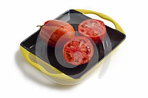 Ripe juicy whole red tomato and halves in a section with seeds on a grill plate, isolated. harvesting the autumn harvest.