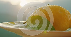 Ripe lemon with a fresh leaves on a ceramic plate, basking in the warm sunlight, background of the Amalfi Coast in Italy