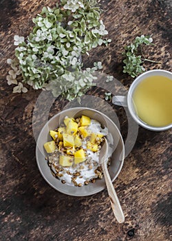 Ripe mango, granola greek yogurt and green tea - delicious breakfast, brunch on a wooden background top view