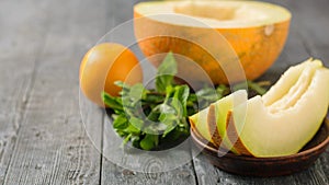 Ripe melon pieces on a clay bowl, banana, mint and orange on a rustic wooden table.