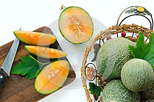 Ripe melons cut into pieces on a wooden board. Whole melons in the basket. White background.