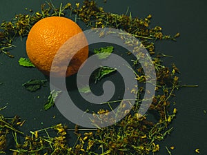 Ripe orange on a dark background. Around the herbs still life close up