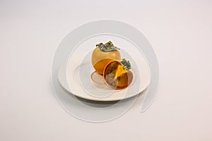 Ripe orange persimmon fruit and persimmon leaves in a blue basket on a brown wooden table