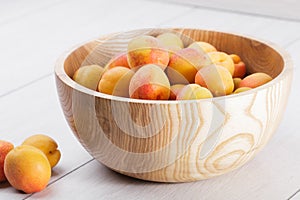 ripe organic apricots fruits in ash tree wooden bowl on a white wooden background