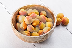 ripe organic apricots fruits in ash tree wooden bowl on a white wooden background