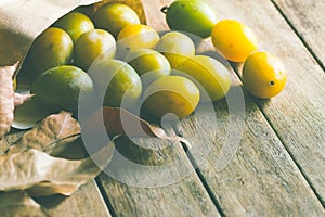Ripe organic colorful yellow and green plums in brown craft paper bag scattered on plank wood background. Dry leaves.