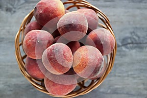 Ripe organic peaches in a brown basket on a gray background