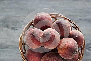 Ripe organic peaches in a brown basket on a gray background