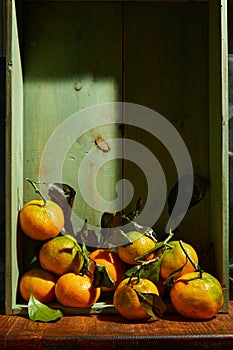 Ripe organic tangerines with leaves in wooden box in bright sunlight with copy space. Natural tropical fruit concept image