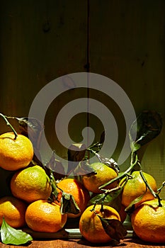 Ripe organic tangerines with leaves in wooden box in bright sunlight with copy space. Natural tropical fruit concept image