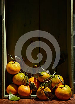 Ripe organic tangerines with leaves in wooden box in bright sunlight with copy space. Natural tropical fruit concept image