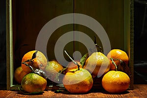 Ripe organic tangerines with leaves in wooden box in bright sunlight with copy space. Natural tropical fruit concept image