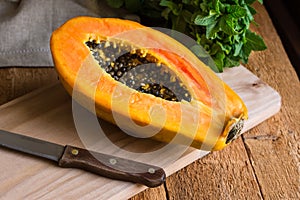 Ripe papaya cut in half on wood cutting board, bunch of fresh mint on rustic kitchen table by window