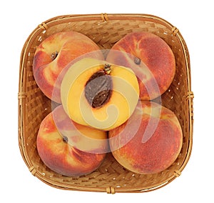 Ripe peach fruit with half in a wicker basket isolated on white background with full depth of field. Top view. Flat lay