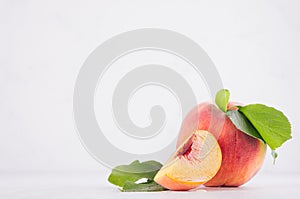 Ripe peach with green leaves, pulpy slice on white light wooden table, copy space.