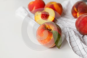 Ripe peaches whole and halved on white checkered fabric on white background