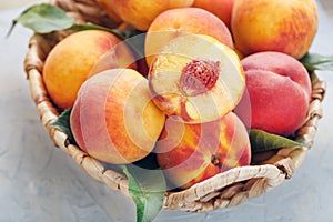 Ripe peaches in a wicker basket on a stone gray table with a juicy peach slice with a stone pit