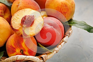 Ripe peaches in a wicker basket on a stone gray table with a juicy peach slice with a stone pit