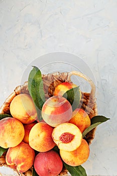 Ripe peaches in a wicker basket on a stone gray table with a juicy peach slice with a stone pit