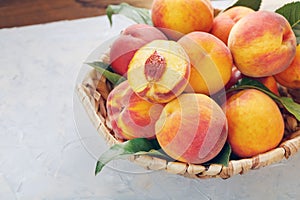 Ripe peaches in a wicker basket on a stone gray table with a juicy peach slice with a stone pit