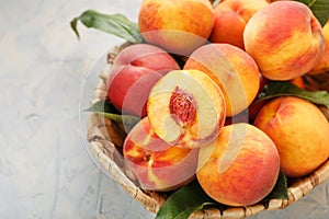 Ripe peaches in a wicker basket on a stone gray table with a juicy peach slice with a stone pit.