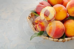 Ripe peaches in a wicker basket on a stone gray table with a juicy peach slice with a stone pit.