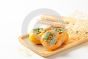 Ripe persimmon fruit in wooden plate on white background