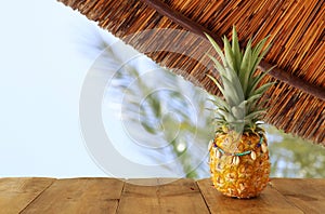 Ripe pineapple over wooden table in front of beach and tropical background