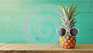 Ripe pineapple in stylish sunglasses over wooden table background. Tropical summer vacation concept. top view