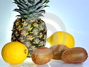 A ripe pineapple with two lemons and three kiwi fruits on white background