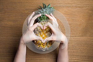 Ripe pineapple with various gestures of women hand make heart shape on wooden background