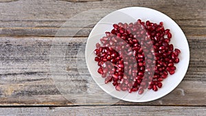 Ripe pomegranate grains in a white  plate isolated on a wooden background. Top view, flat lay.