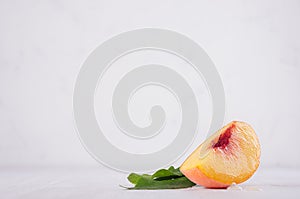 Ripe pulpy peach slice with green leaves on white light wooden table, copy space.