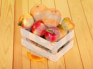 Ripe pumpkins and apples in box on background light wood.