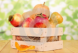 Ripe pumpkins and apples in wooden box on abstract green background.