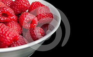 Ripe raspberries in a white bowl on a black background