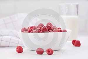 Ripe raspberries in white bowl and glass of milk