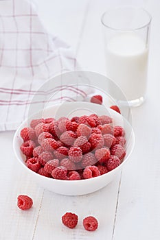 Ripe raspberries in white bowl and glass of milk