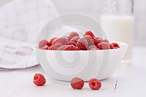 Ripe raspberries in white bowl and glass of milk