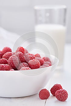 Ripe raspberries in white bowl and glass of milk