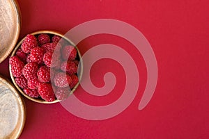 Ripe raspberries in a wooden container on a red background. Copy Space